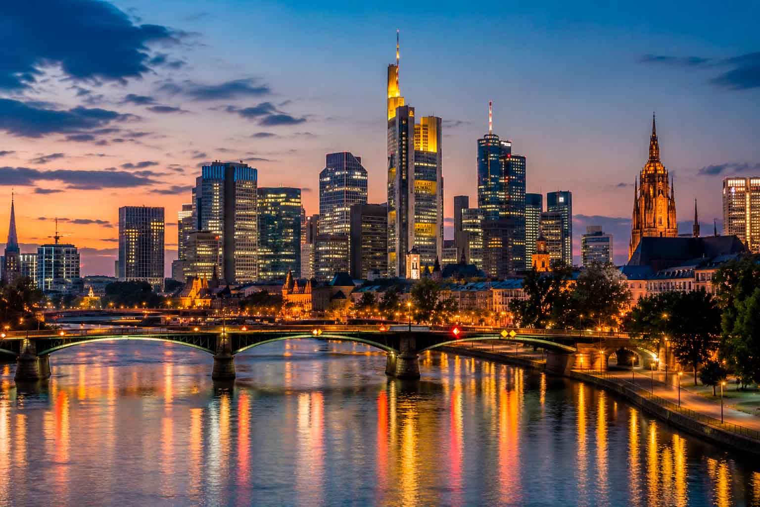 Frankfurt skyline at dusk with illuminated financial district buildings and river reflections, used as a regional context image for data center photographer services.